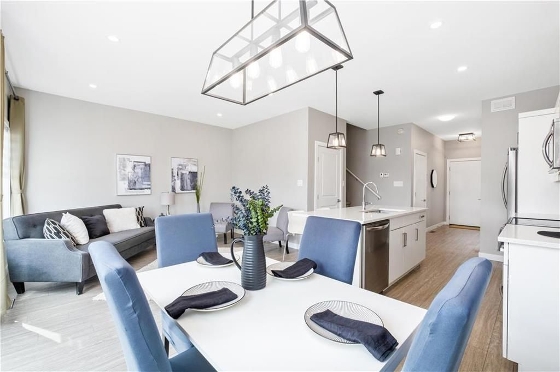 Interior of  340 John Angus Drive in South Pointe, Winnipeg. An open concept with the dinning area, living room, and kitchen with an island all in view. Light grey colour scheme with quartz counter tops. Blue accents throughout the home: the dinning room chairs, napkins, and in the living rooms artwork. Chestnut floors throughout.  