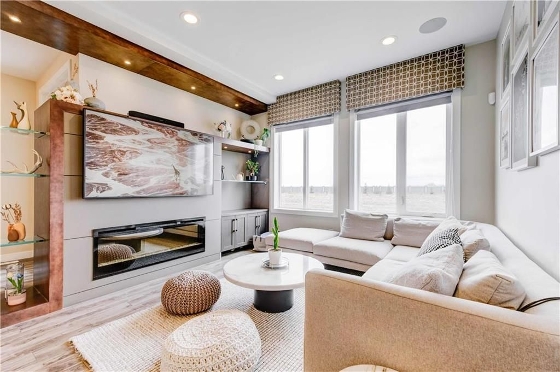 Living room of 247 Park East Drive in Bridgwater Centre, Winnipeg. Spacious, beige colour scheme, a large L shaped couch along the back wall, built in shelving and an entertainment centre against the opposite wall, two large windows, and in ceiling lighting. 