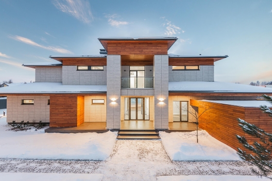 A beautiful house during the winter. House is made of white stone and wood accents. Bright blue sky.